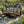 Japanese Bridge with Split Railings 12 ft Taiko spans a small pond with water lilies and waterfalls in a sunny spring garden.