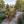 A rustic wooden bench with decorative wheels on the sides sits on a stone path in a beautifully landscaped garden with mountains in the background.