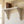 A white decorative wall shelf mounted on a cream-colored wall, with three brown books, a brass candlestick, and a teacup.
