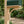 Close-up of a wood corbel supporting a dark green mailbox, with blurred greenery in the background.