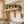 Light natural wood wall shelves mounted on a cream subway tile kitchen wall, styled with multiple potted green herbs and trailing plants.