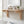 A light natural wood bathroom shelf mounted on a beige wall above a white tub, styled with folded white towels, a glass jar, soap bars, and a small potted succulent.
