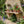 A rustic garden shelf holding several terracotta potted plants with flowers and greenery against a stone wall in a garden.